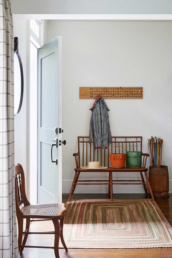 entry in a home filled with a spindle backed deacon's bench with antique tins sitting on it. There's an antique peg game being used as a coat rack.