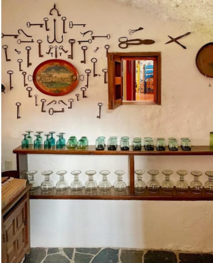 casa de la torre in spain with one wall showing a collection of antique keys next to a wood framed window. Below that are wood shelves with clear and green glasses.