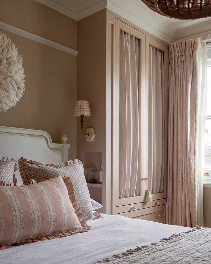 pale pink bedroom designed by sean symington and showcases a built in combo nightstand and wardrobe. The wardrobe doors are covered in gathered fabric.