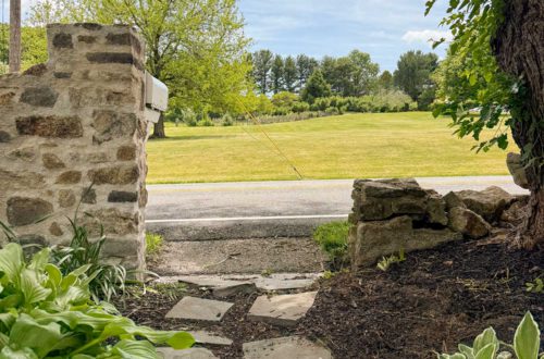 flagstone path on mulch leading to a fieldstone wall that is newly rebuilt on the left side but still waiting to be rebuilt on the right side