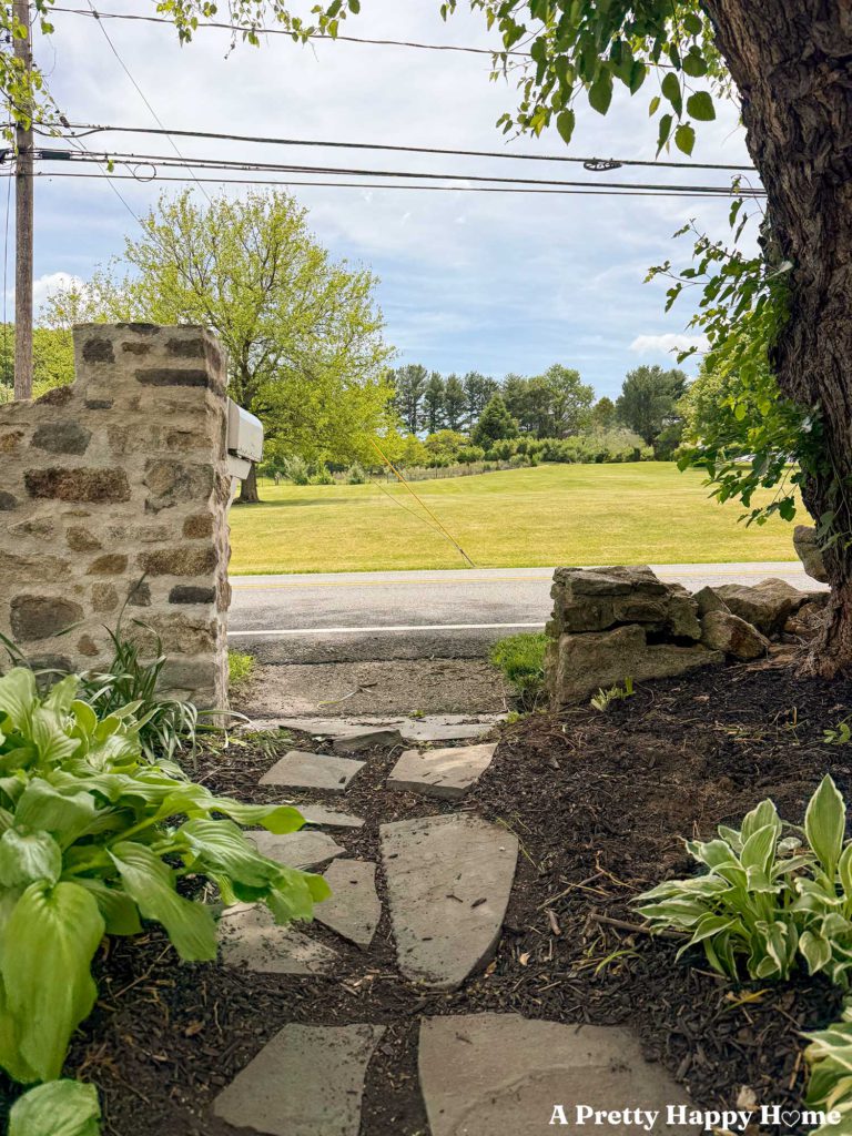 flagstone path on mulch leading to a fieldstone wall that is newly rebuilt on the left side but still waiting to be rebuilt on the right side