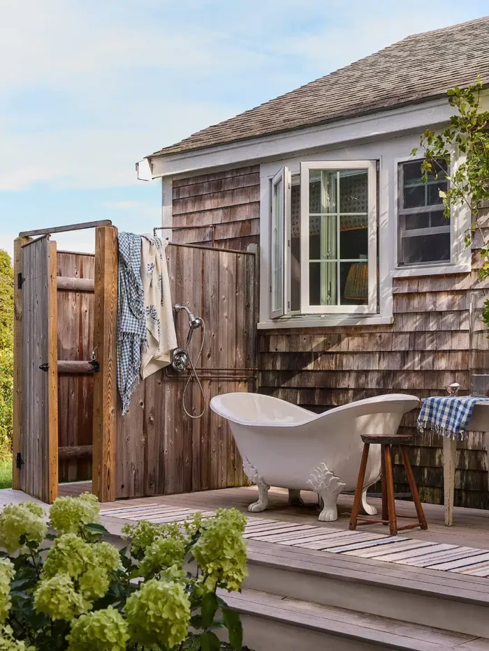 Genevieve Lavelle-Brewster Home Tour on Cape Cod showing an outdoor clawfoot white bathtub sitting on a deck next to an outdoor shower on a shingled cape cod style home