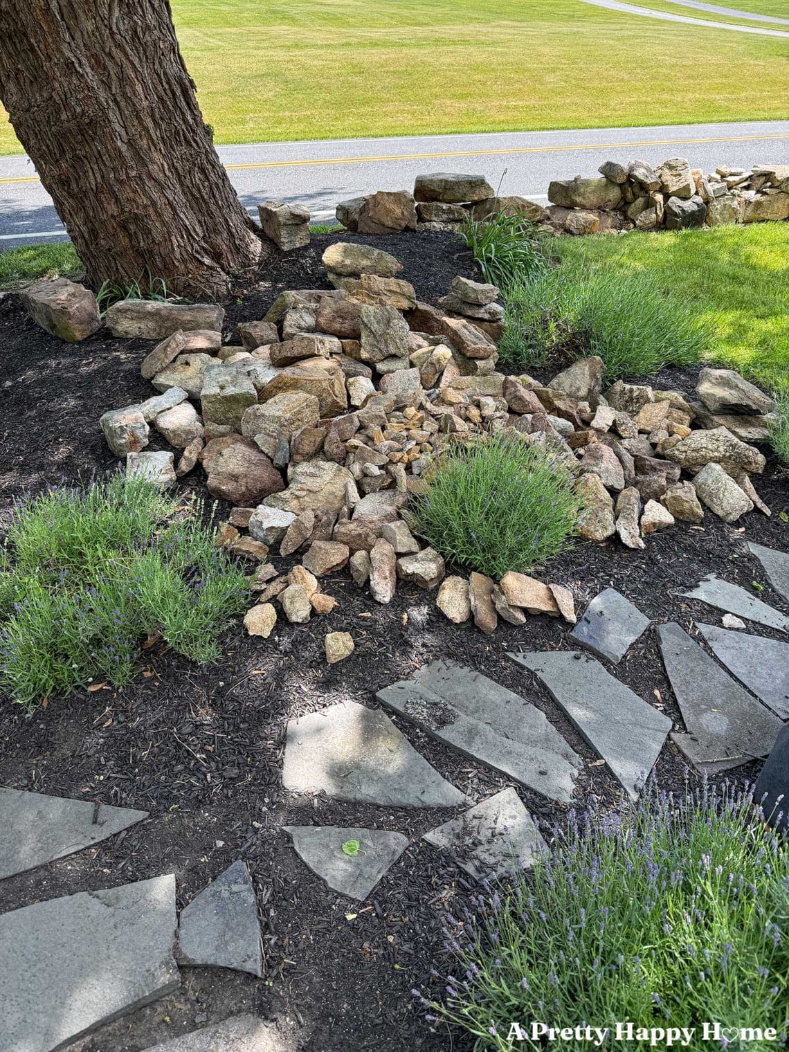 Pile of fieldstone rocks in a flower bed that have been demoed from a nearby low stone wall that will be reconstructed
