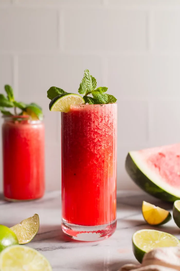 watermelon slushie in a tall glass garnished with lime wedge and mint