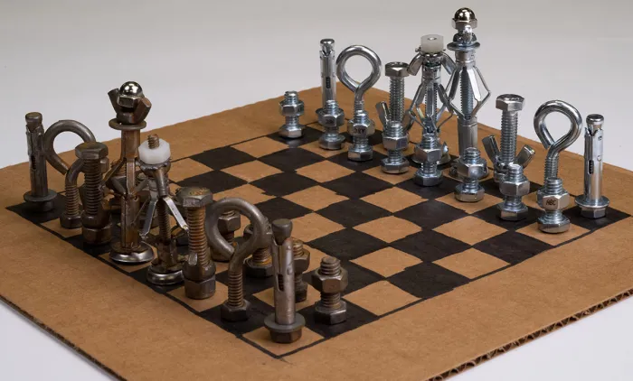 chess set made from old hardware like nuts and bolts and sitting on a cardboard chess board