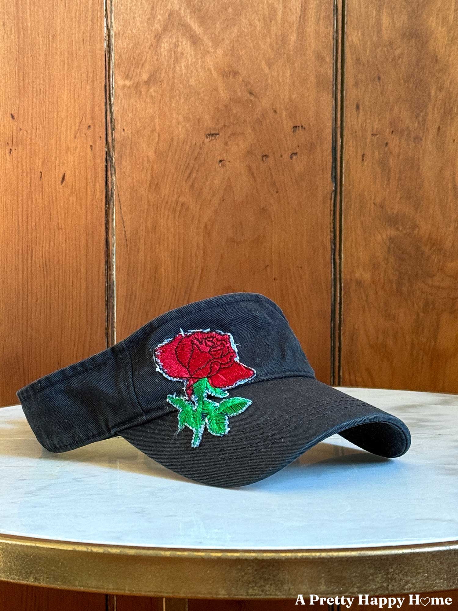 black visor with a red rose patch on the side of the headband sitting on a white table