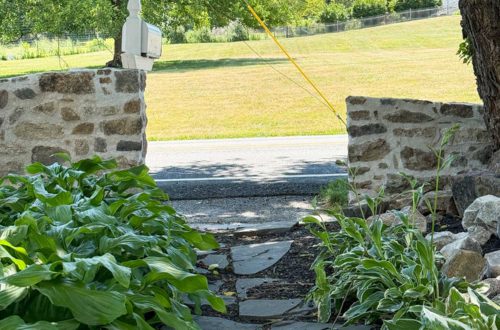 Two sloped fieldstone walls of different heights separated in the middle by a flagstone path