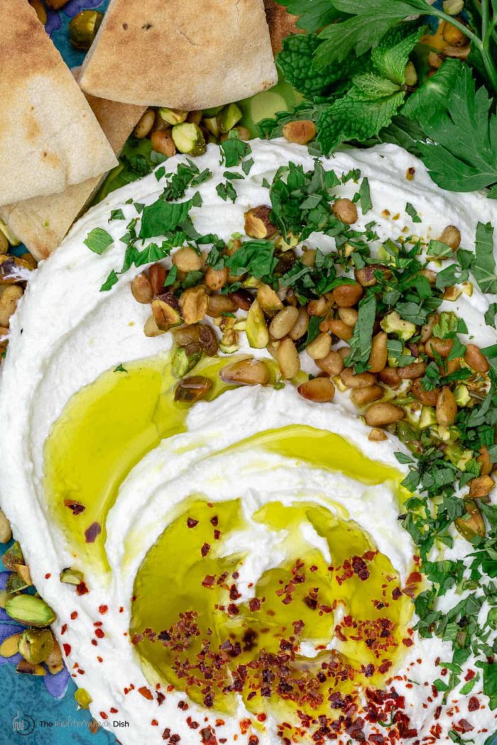 close up of a creamy whipped feta dip with olive oil, pine nuts, and herbs drizzled on top
