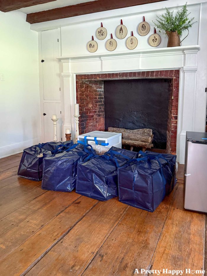 blue bags packed for college in front of a fireplace with wood rounds stamped with leaves hanging above the mantel