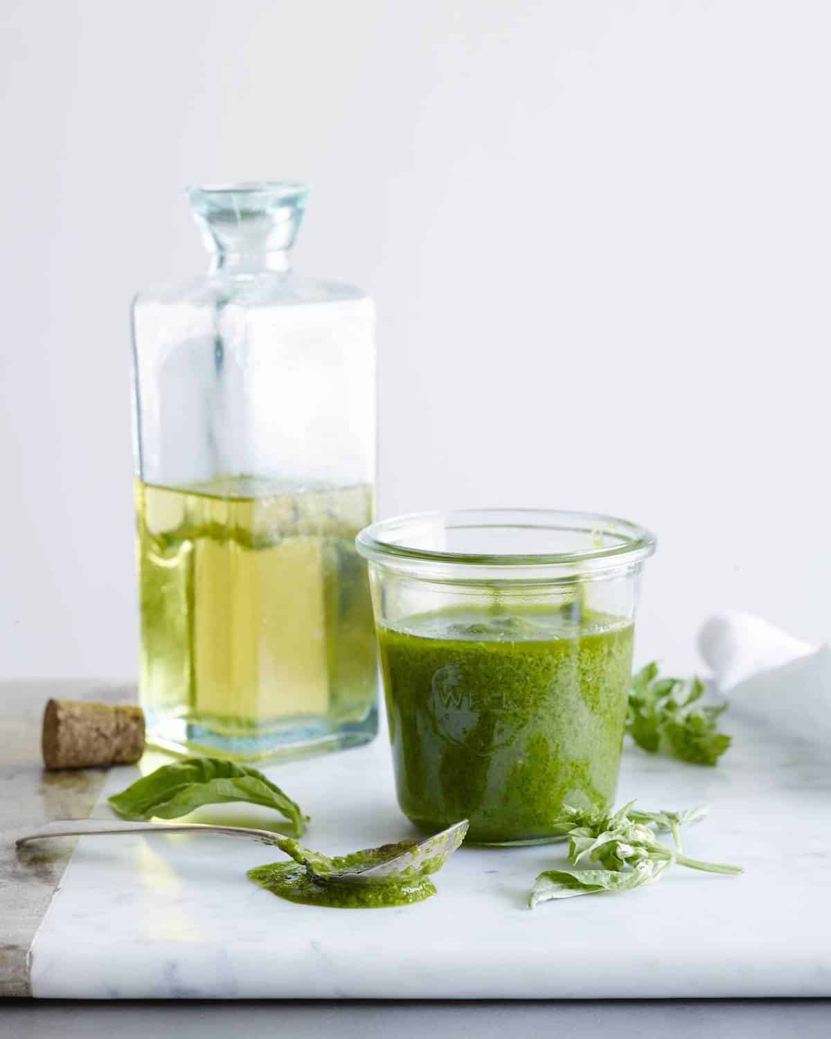 jar of homemade basil vinaigrette sitting in front of a bottle of olive oil