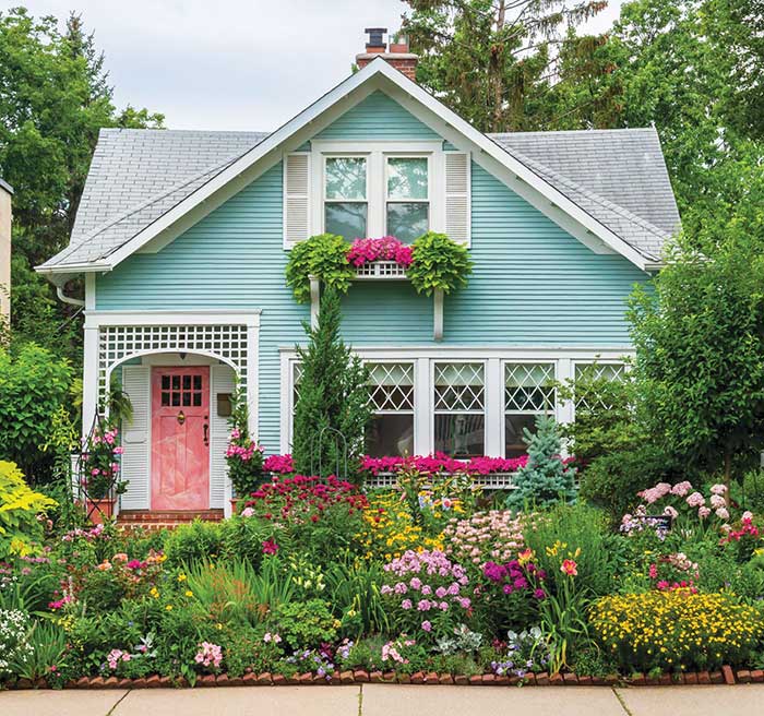 storybook looking house with turquoise trim, pink front door, flower boxes, and a flower garden in front.
