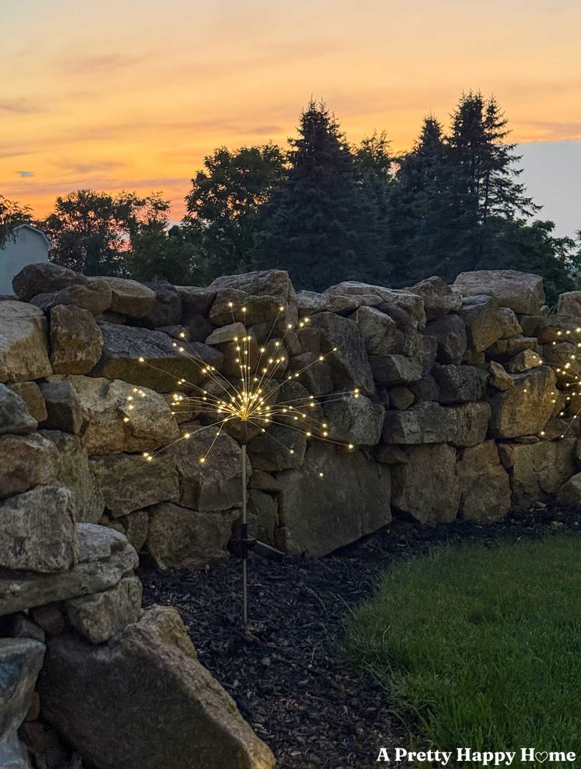 sparkler solar light in front of a stone wall with an orange sunset in the background