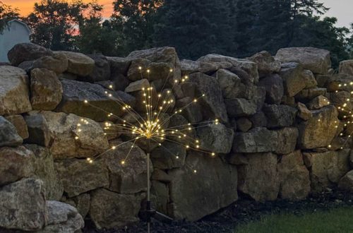 sparkler solar light in front of a stone wall with an orange sunset in the background