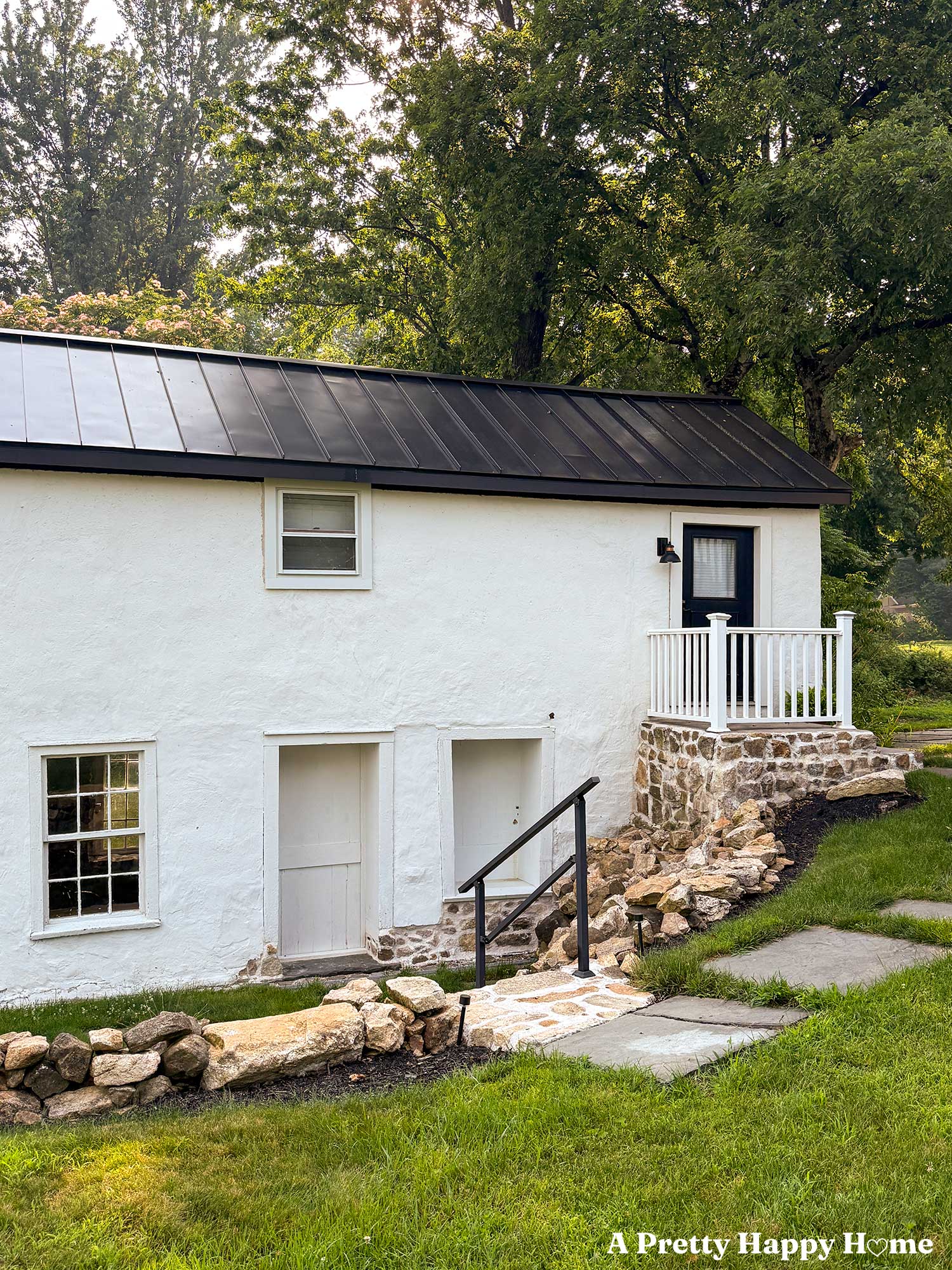 white carriage house with black metal roof and stone porch showcasing new window trim on an upper window
