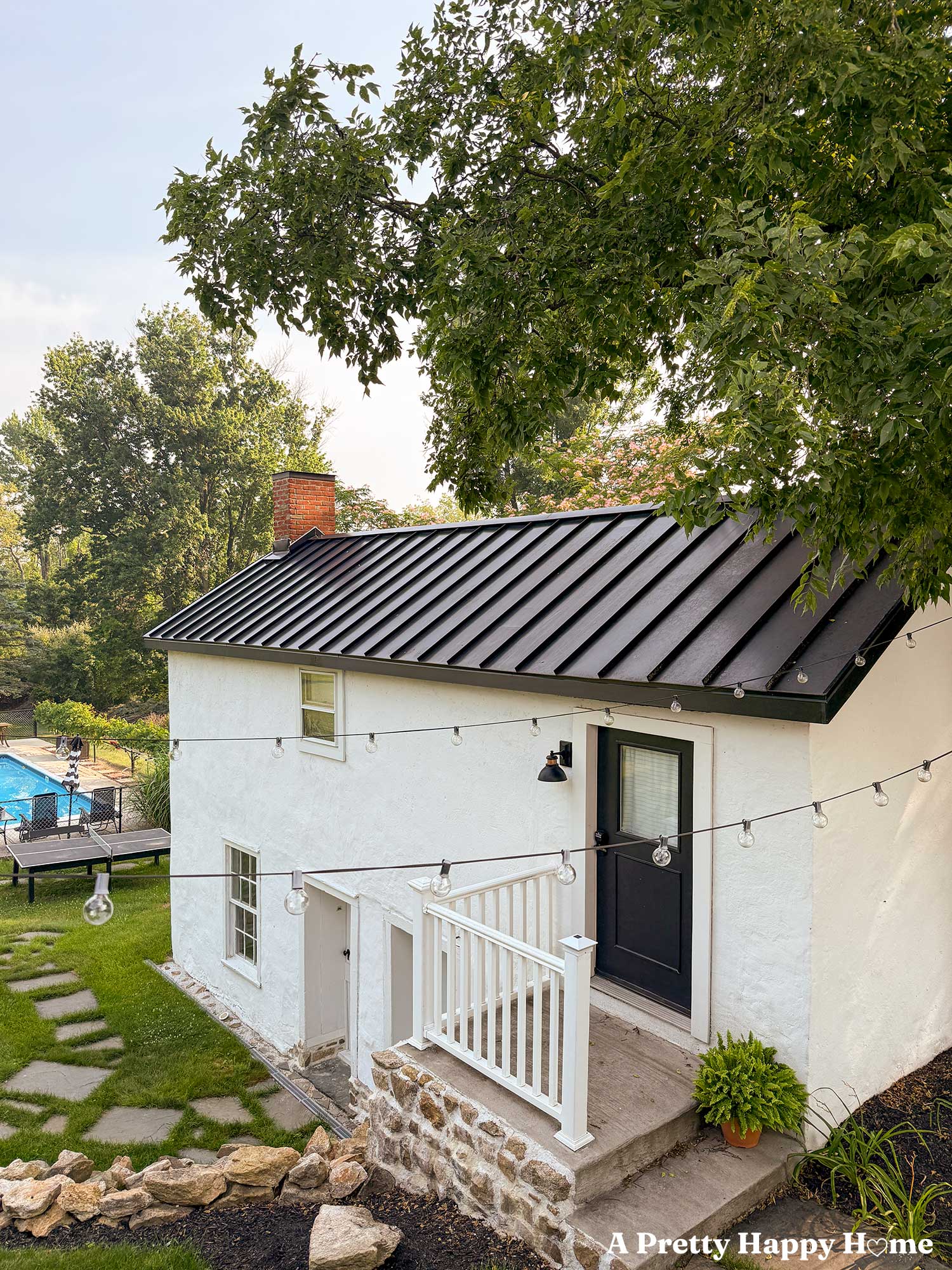 white carriage house with black metal roof and stone porch showcasing new window trim on an upper window