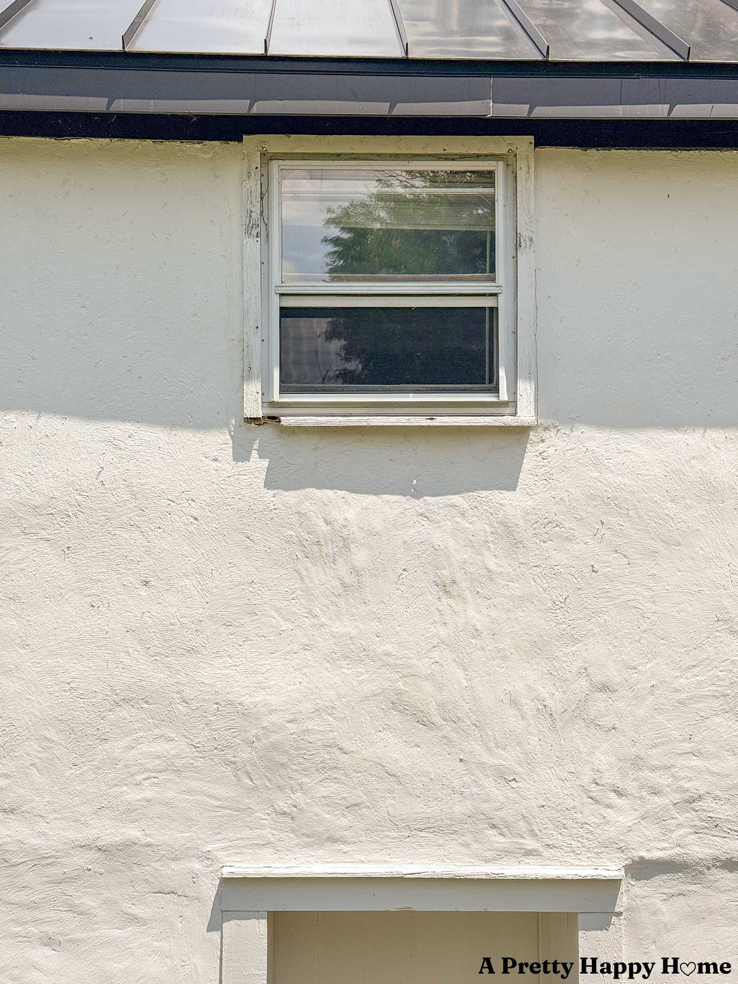 rotten window trim on a white stone building with a black metal roof