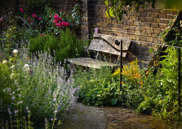 wood bench with a curved back detail that sits in an english garden against a brick wall
