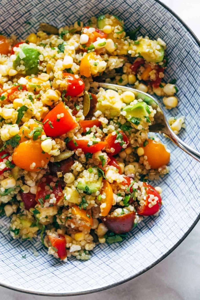corn, avocado, and quinoa salad plated in a large bowl and sprinkled with green herbs and tomatoes