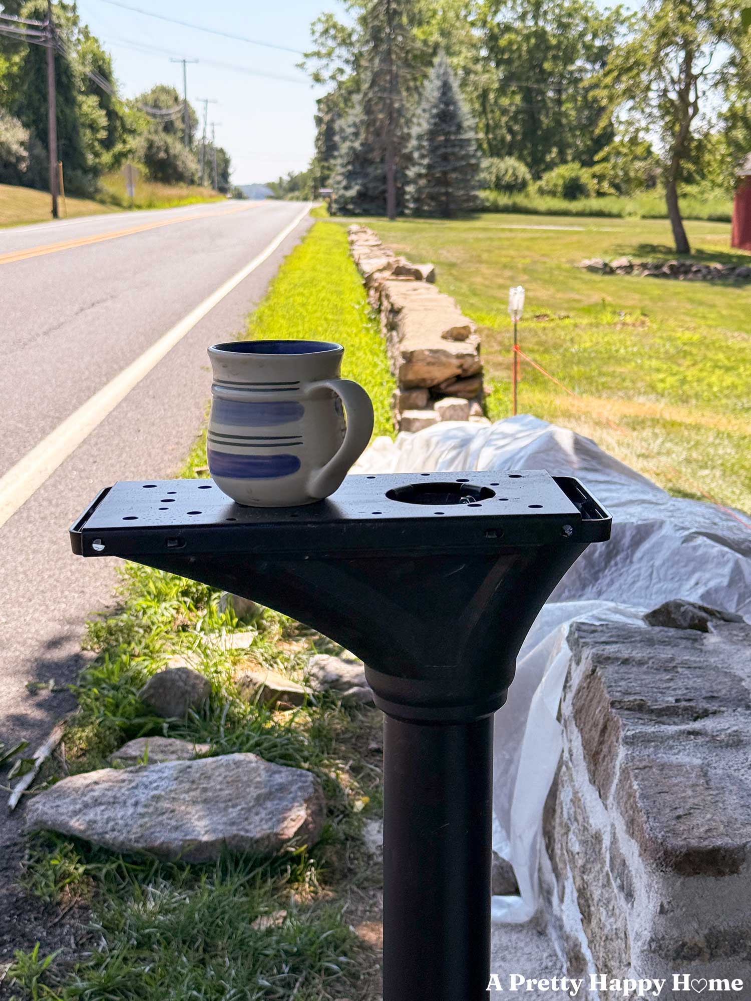 cup of coffee sitting on a mailbox post while it waits for the mailbox itself to be installed. Low stone wall in the background is under construction.