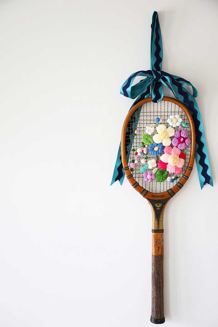 vintage tennis racket with flowers embroidered on it and hung from a turquoise and black ribbon
