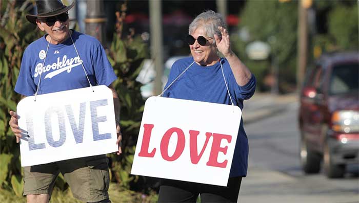 two elderly people, man and woman, wearing blue shirts with big love signs hanging around their necks