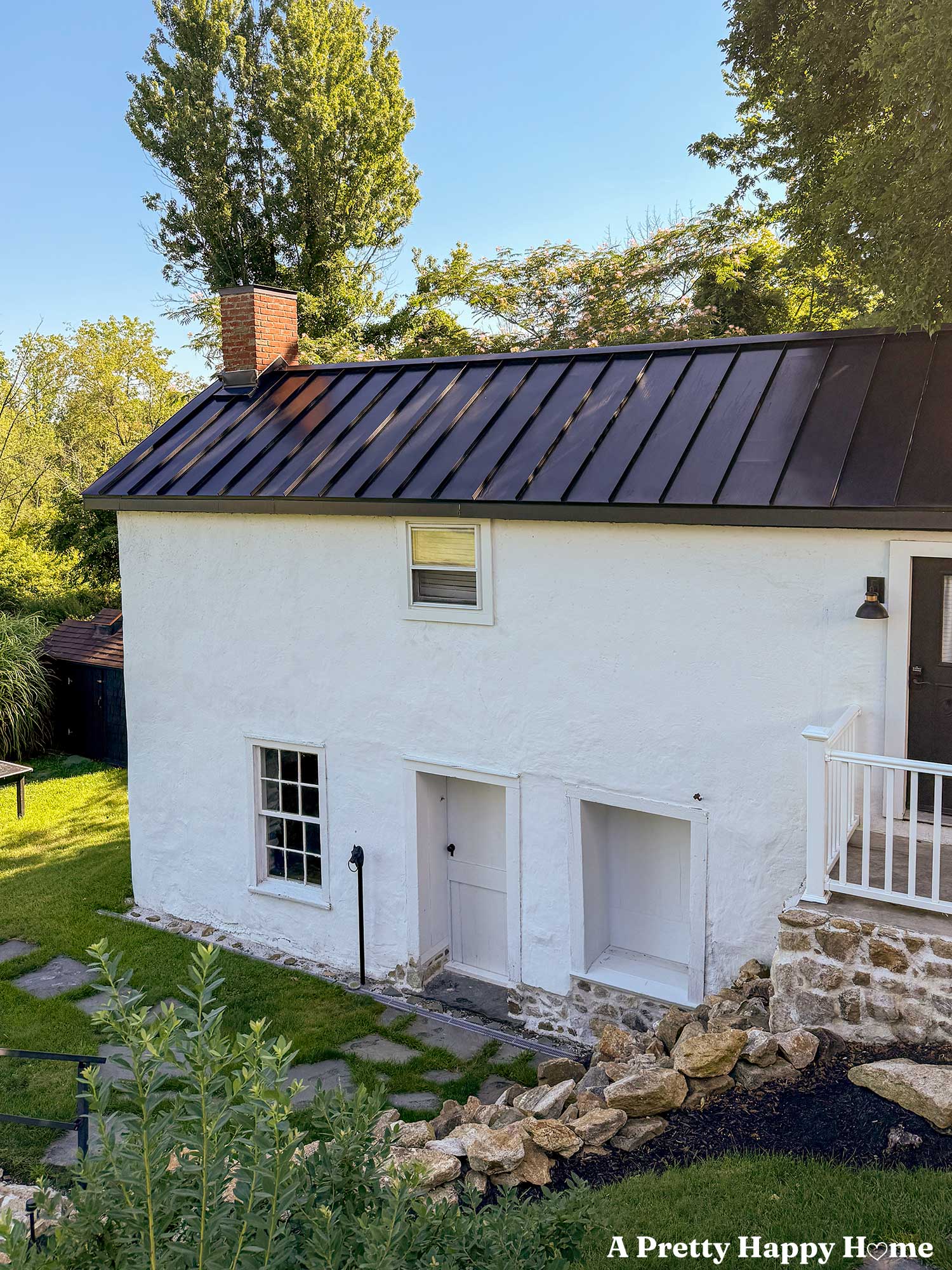 antique cast iron horse head hitching post installed in front of a white carriage house with a black metal roof. There's a flagstone path set in grass around the hitching post and the building has a stone wall and foundation.