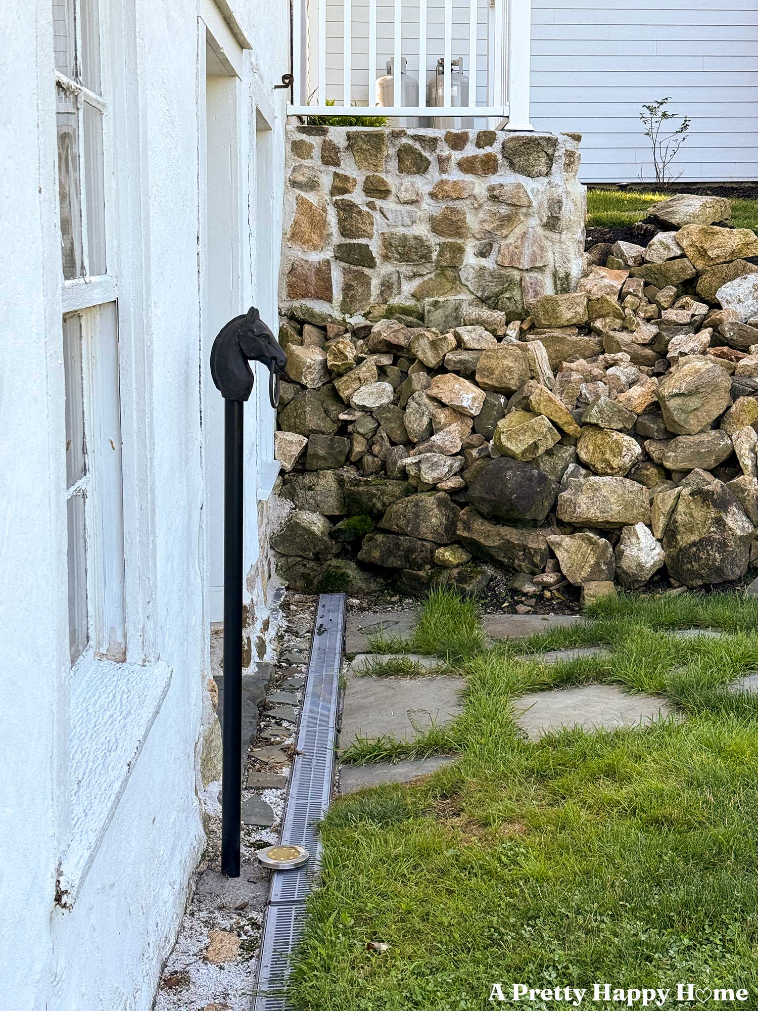 antique horse head hitching post installed in front of a white carriage house and in the background is a stone wall