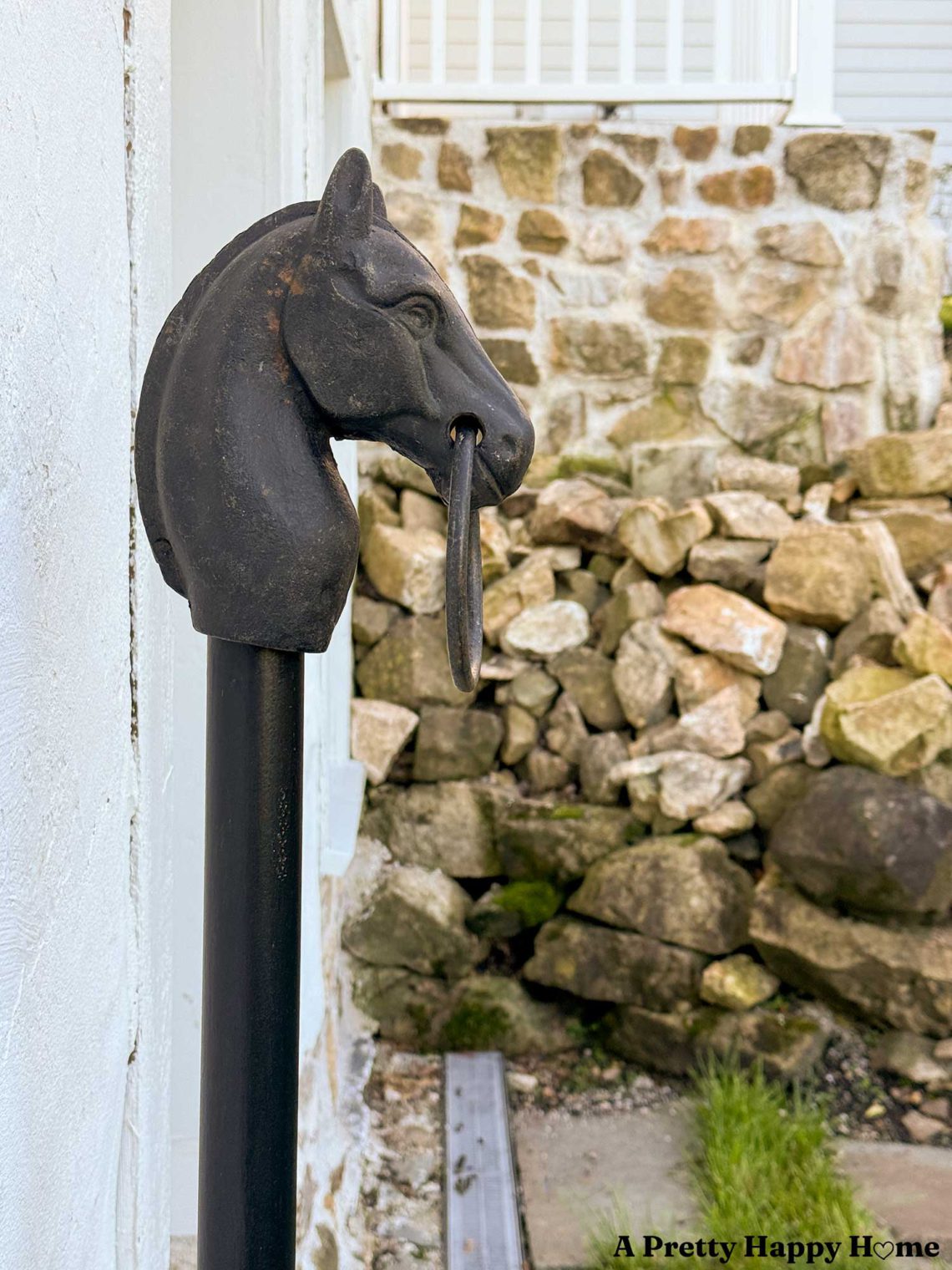 antique cast iron hitching post installed in front of white carriage house with a stone wall in the background