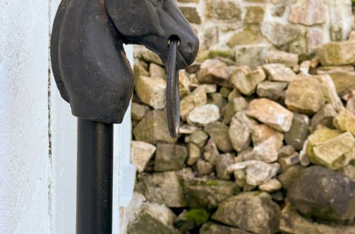 antique cast iron hitching post installed in front of white carriage house with a stone wall in the background