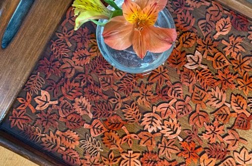 Fall-Themed Resin Tray With Wood Leaf Cutouts the tray is wood and lighter colored wood leaf cutouts line the bottom of the tray and look like they are floating in the resin. A tiny glass vase with orange flowers sits on the tray.