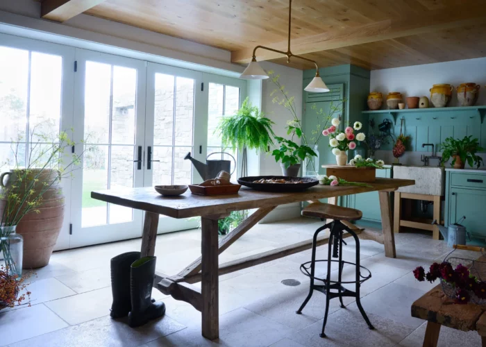 garden room in the basement of a 19th century farmhouse in vermont with french doors, limestone floors, green cabinets, and a floating work table in the center of the room.