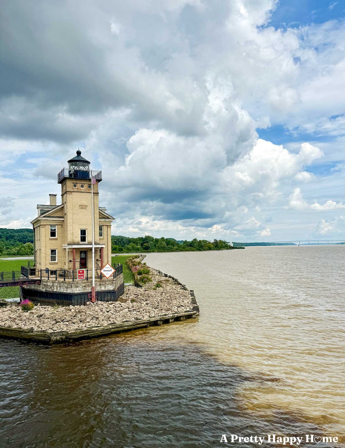 tac colored lighthouse sitting on the edge of the hudson river in kingston, new york. The sky is partly cloudy and the river is very muddy after a recent storm.