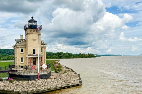 tac colored lighthouse sitting on the edge of the hudson river in kingston, new york. The sky is partly cloudy and the river is very muddy after a recent storm.