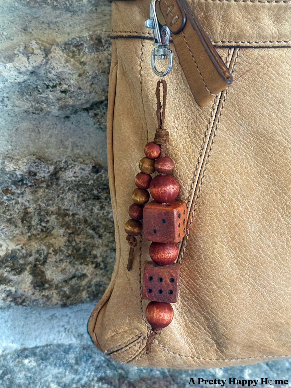 bag charm hanging from a tan leather bag that is made of round wood beads in a mahogany color and two wood dice also in a mahogany color