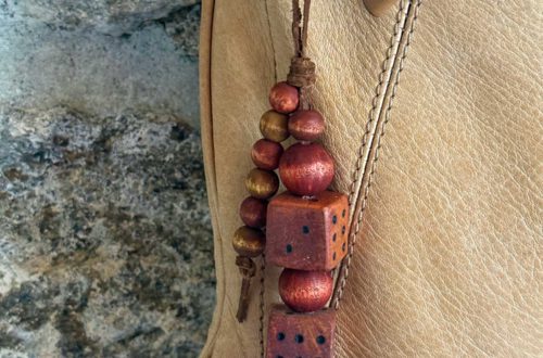 bag charm hanging from a tan leather bag that is made of round wood beads in a mahogany color and two wood dice also in a mahogany color