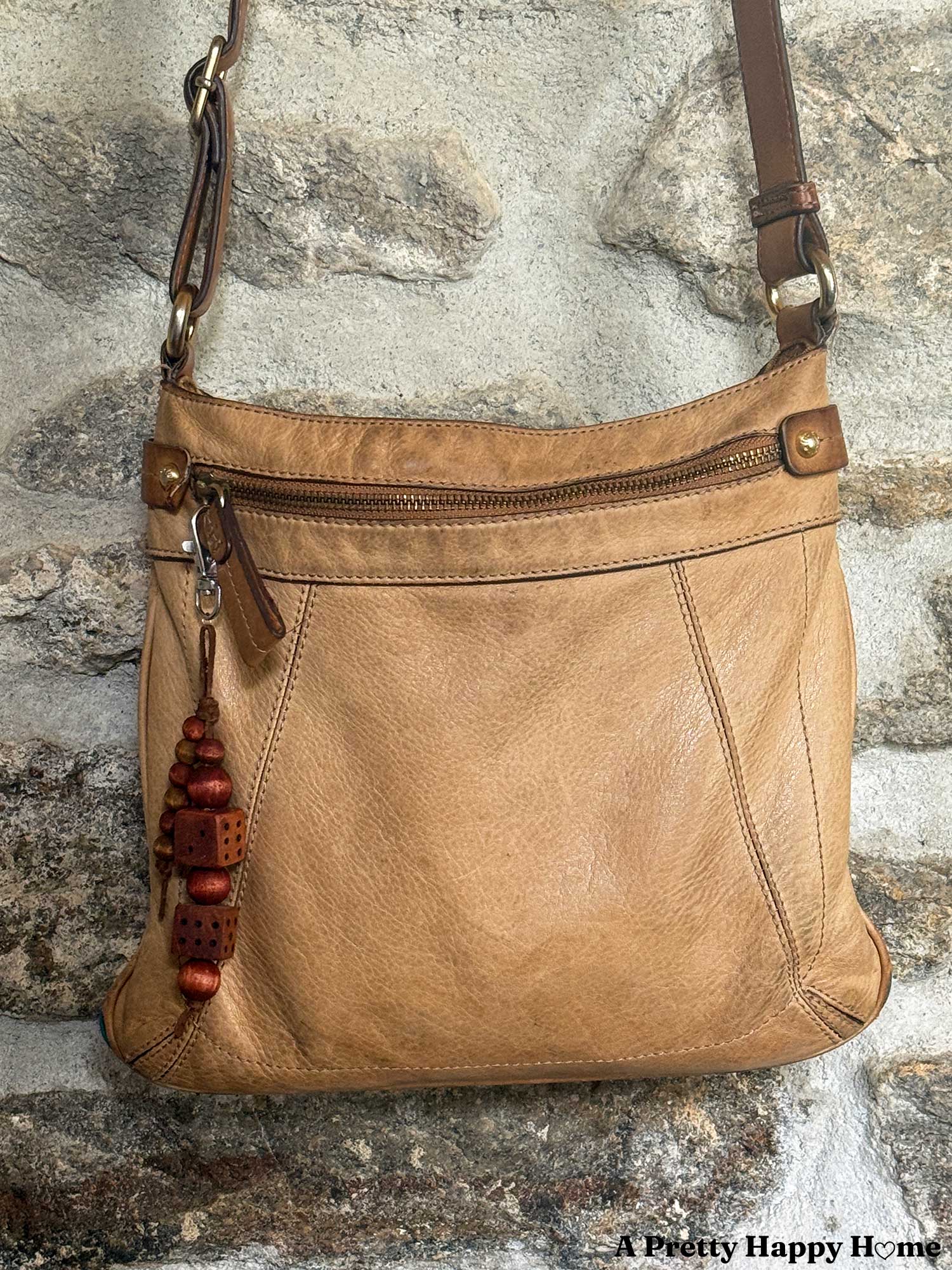 bag charm hanging from a tan leather bag that is made of round wood beads in a mahogany color and two wood dice also in a mahogany color