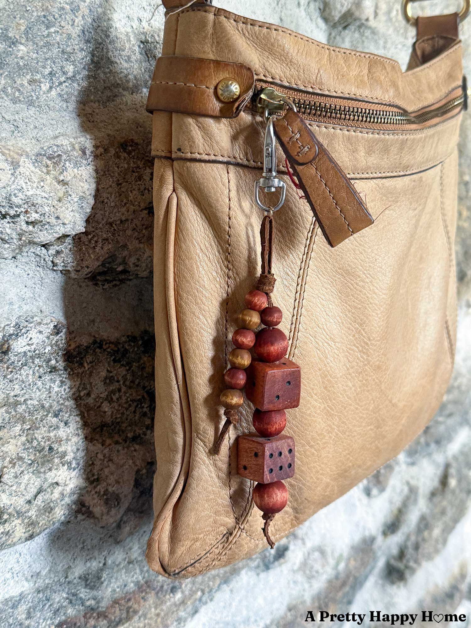 bag charm hanging from a tan leather bag that is made of round wood beads in a mahogany color and two wood dice also in a mahogany color