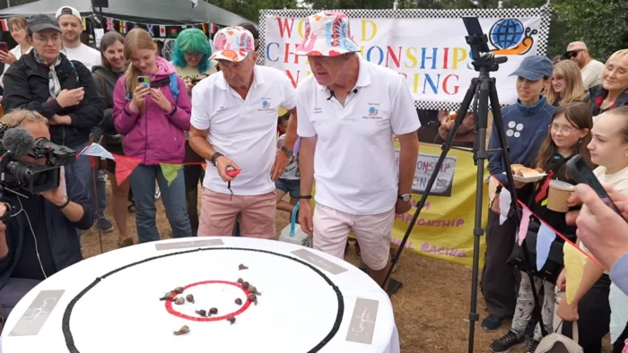 "Snail Master" Ian Haynes on the left surrounded by a crowd cheering on snails at the world snail racing championship in 2026 in Norfolk