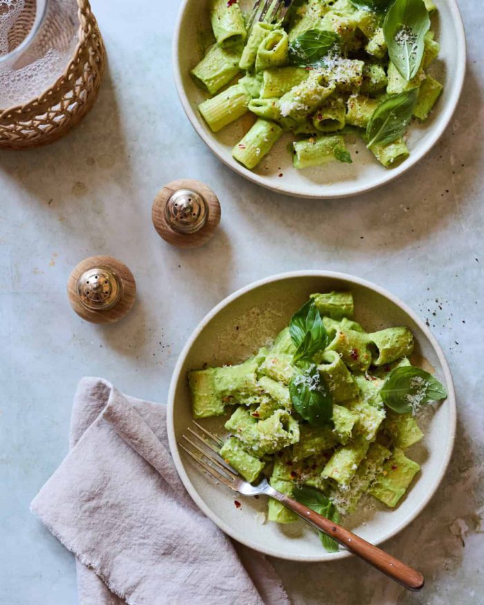 two bowls of zucchini pasta topped with basil leaves next to gold salt and pepper shakers and cloth napkins