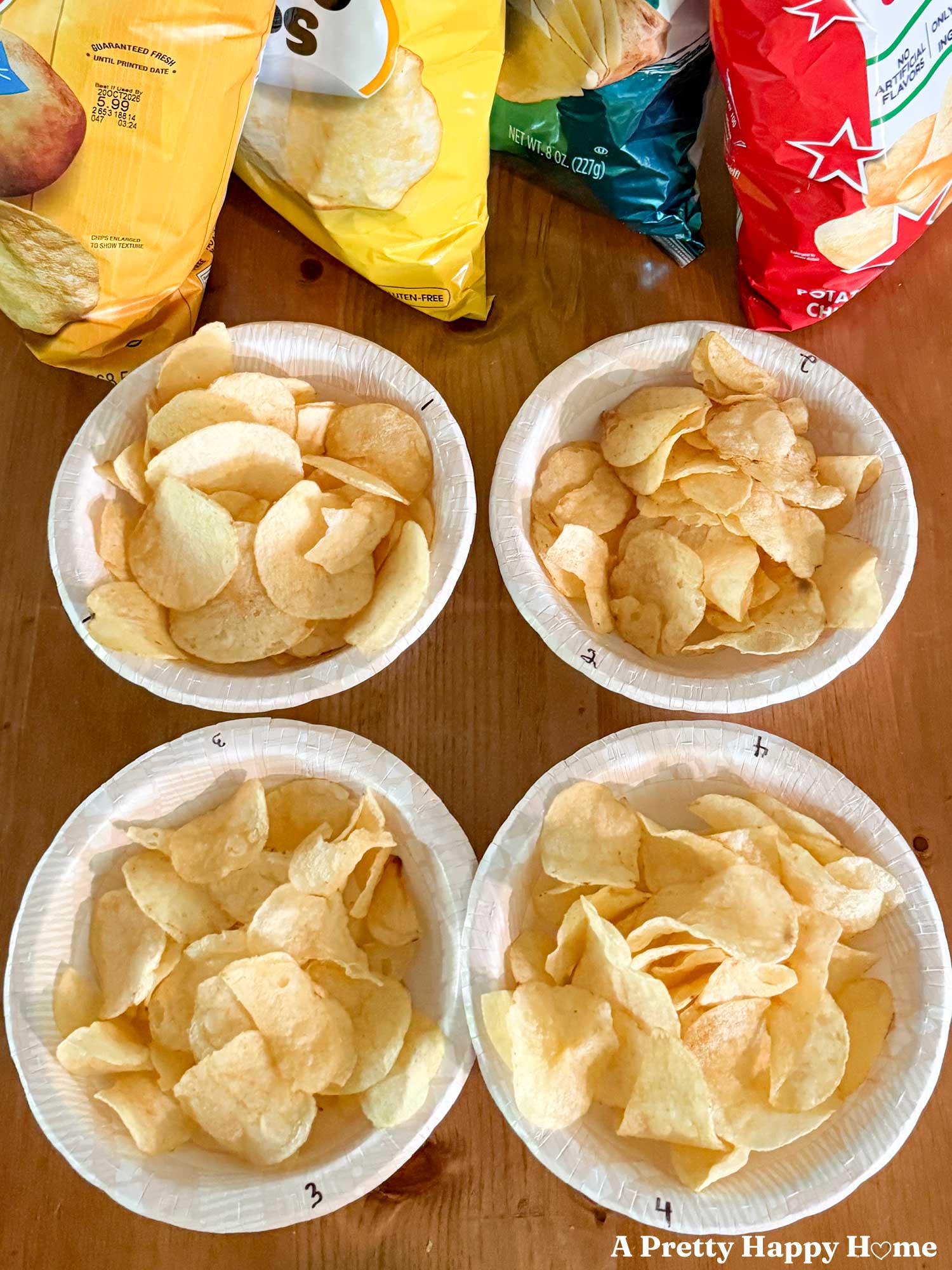 four bags of chips sit obscured behind four numbered paper bowls holding classic potato chips for a blind taste test